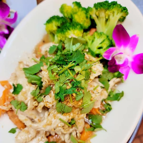 Elephant Thai's garlic chicken with broccoli, carrots, and cilantro, garnished with a purple orchid.