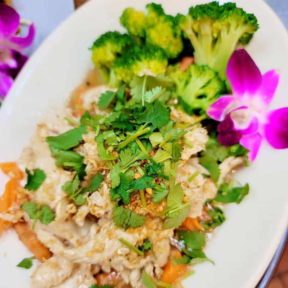 Elephant Thai's garlic chicken with broccoli, carrots, and cilantro, garnished with a purple orchid.
