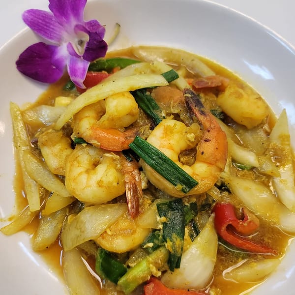 Close-up of Elephant Thai's yellow curry with shrimp, onions, and green vegetables, garnished with a purple orchid.